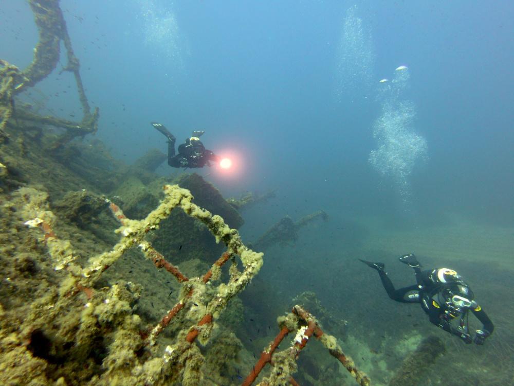 Two scuba divers with a torch light next to shipwreck